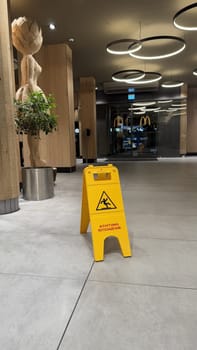22.03.2025 Germany: Indoor McDonalds Setting Featuring a Caution Sign and Wooden Decorative Art Piece. Modern interior of McDonalds with clean floors, wooden decor, and a bright yellow caution sign emphasizing safety.