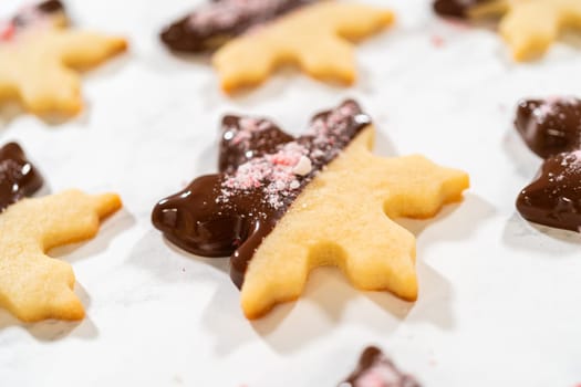 Close-up of a chocolate-dipped snowflake sugar cookie topped with crushed peppermint candy on parchment paper.