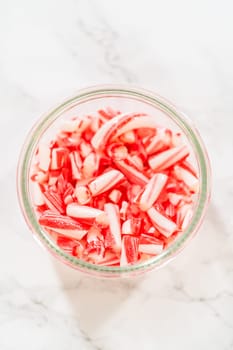 A glass jar filled with crushed candy canes, displayed on a marble countertop, showcasing their vibrant red and white stripes for holiday dessert decoration and baking.