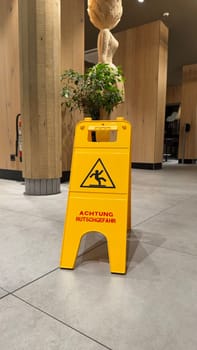 25.03.2025 Germany: Yellow Caution Wet Floor Sign Displayed on Modern Indoor McDonalds Tile Flooring. Detailed close-up view of a warning sign in a stylish modern interior, alerting pedestrians to potential slipping hazards on the tile surface.