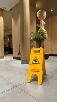 25.03.2025 Germany: Caution Wet Floor Sign in Modern Wooden Interior with Decor in McDonalds. Bright yellow caution wet floor sign displayed on tiled floor in a cozy wooden interior with decor.