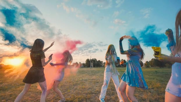 Young women celebrating holi festival, throwing colored powder in the air at sunset, enjoying friendship and togetherness