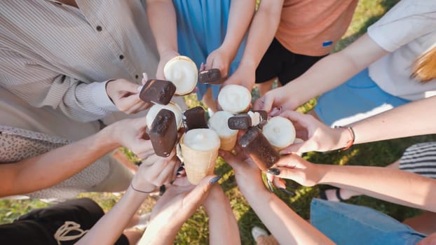 School friends are holding ice cream cones and chocolate covered ice cream bars, enjoying a sweet treat together outdoors
