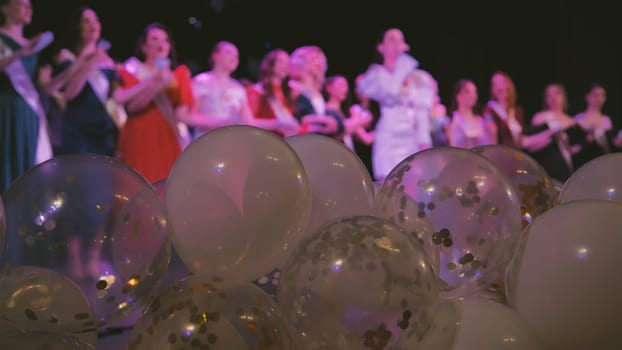 White and transparent balloons decorated with confetti during a school event with a group of clapping friends in the background
