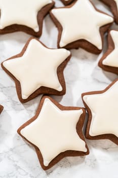 A neat arrangement of gingerbread star cookies covered in white royal icing, emphasizing their festive and uniform design.
