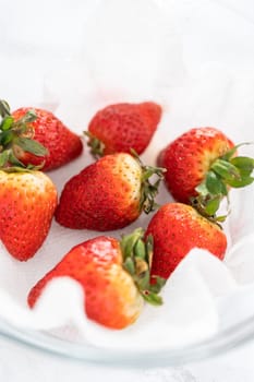 Freshly washed and dried strawberries are carefully arranged in a glass bowl lined with paper towel, ready for snacking or further use.