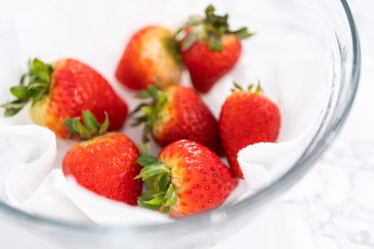 Freshly washed and dried strawberries are carefully arranged in a glass bowl lined with paper towel, ready for snacking or further use.