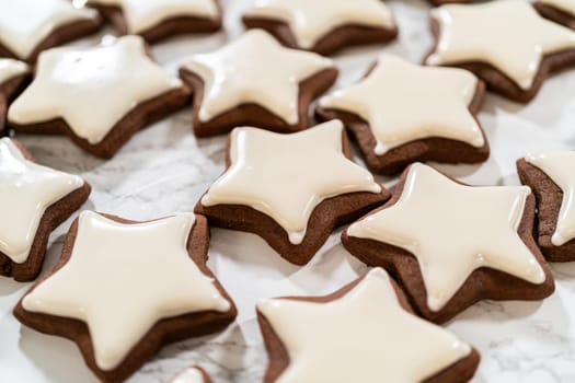 A neat arrangement of gingerbread star cookies covered in white royal icing, emphasizing their festive and uniform design.