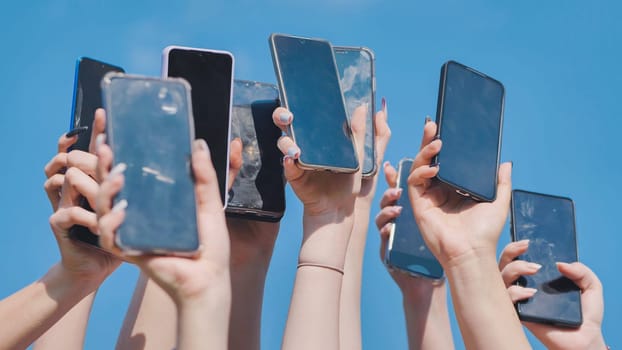 Hands holding mobile phones with blank screens against blue sky, symbolizing communication, technology, and social media in education