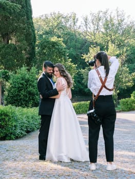 Photographer girl photographs bride and groom hugging in the garden. High quality photo