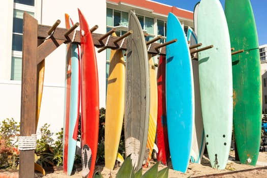 Many Surfboards On Stand Outdoor. Colorful Soft Foam And Wooden Construction Classic Surfboard Longboard Or Malibu. Horizontal. Sunny Day, Seashore Or Ocean. Nobody. High quality photo