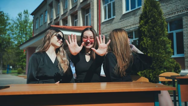 Three happy teenage students smiling and showing their hands to the camera, enjoying a sunny day outdoors after school