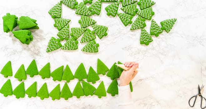 A detailed flat lay showing a mix of decorated and undecorated Christmas tree cookies on a marble surface. The decorated cookies feature intricate royal icing patterns, creating a festive and elegant display.