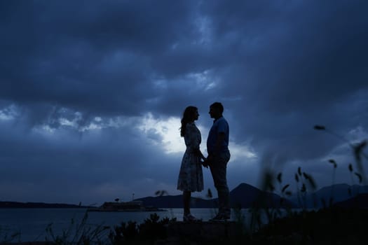 Man and woman stand holding hands by the sea against a dark sky. High quality photo