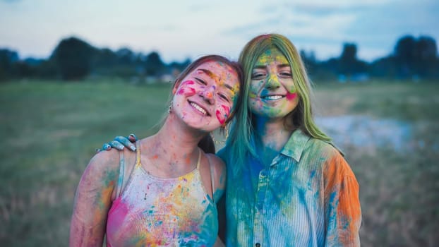 Two young women, adorned in colorful holi powder paint, hug and smile, rejoicing in friendship and the happiness of the festival