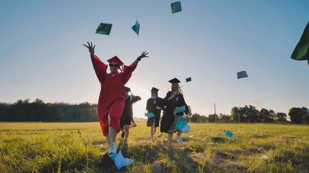 Group of cheerful graduates wearing gowns and caps throwing books in the air, celebrating their academic achievement