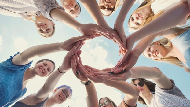 Group of school friends forming a circle with their hands against a blue sky, symbolizing unity, teamwork, and friendship
