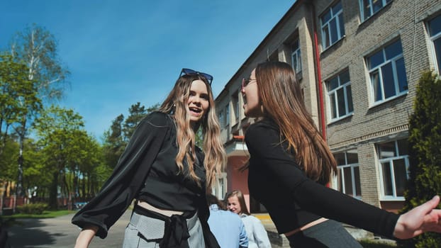 Two happy students are enjoying a lively conversation outside their school on a sunny day, sharing laughter and excitement