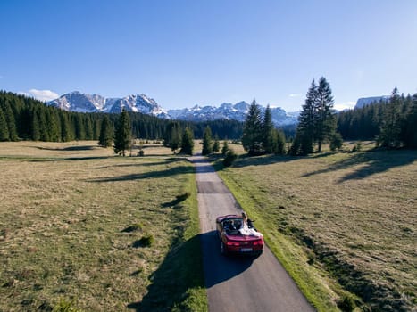 Bride and groom are riding in a red convertible along the road in a mountain valley. Drone. High quality photo