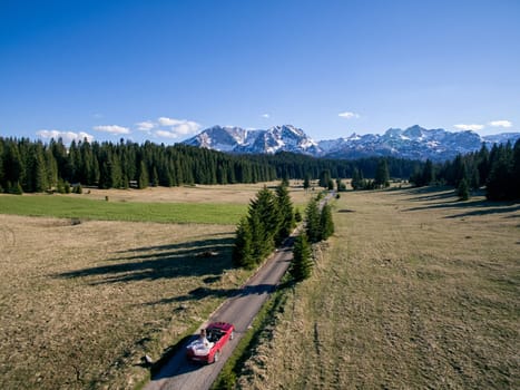 Bride and groom are driving along the highway in the mountains in a red cabriolet. Side view. Drone. High quality photo