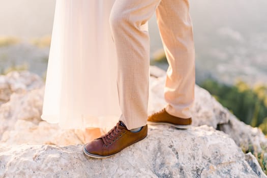 Feet of bride and groom stand on the rock. Cropped. Faceless. High quality photo