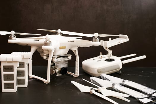 White DJI Phantom 3 UAV with spare batteries, propellers and control panel stands on a black table. High quality photo