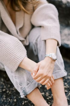 Girl in a sweater and jeans sits with her hands folded on her knees on stone steps. Cropped. Faceless. High quality photo