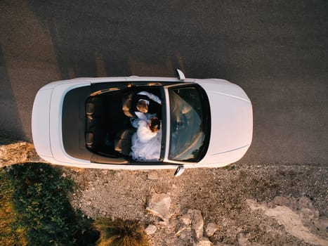 Bride and groom are driving in a white convertible on the highway. Top view. High quality photo
