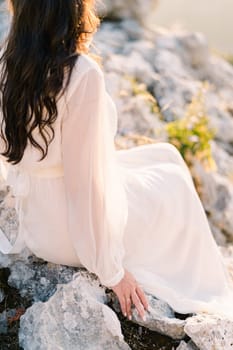 Bride sits on a rocky mountain in the sun. Side view. Cropped. High quality photo