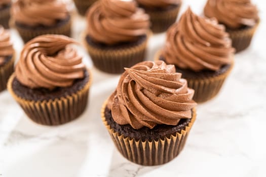 Delicate swirls of rich chocolate icing are meticulously piped onto each chocolate cupcake, creating an irresistible treat.