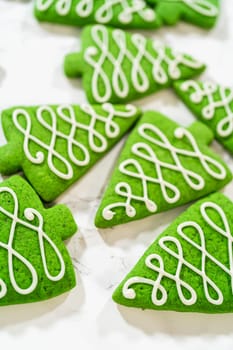 Close-up of green Christmas tree cookies with intricate white icing swirls, emphasizing the smooth texture and precise decoration.