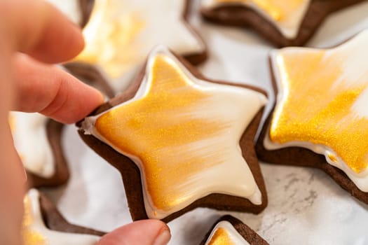 A hand holding a gingerbread star cookie coated in royal icing and painted with gold luster dust, showcasing its intricate and festive design.