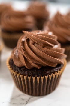 Delicate swirls of rich chocolate icing are meticulously piped onto each chocolate cupcake, creating an irresistible treat.