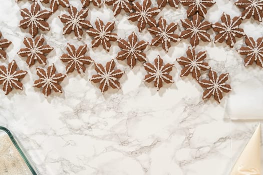 A wide shot of dozens of chocolate ginger snowflake cookies, some decorated with royal icing and sugar crystals, laid out neatly on a marble surface in a festive arrangement