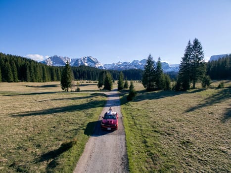 Bride and groom are riding in a cabriolet along a highway in a mountain valley. Drone. High quality photo