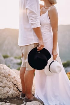 Groom and bride standing in the mountains with hats in their hands. Cropped. Faceless. High quality photo