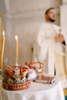 Wedding crowns lie next to the lit candles on the table in the church near the priest. High quality photo