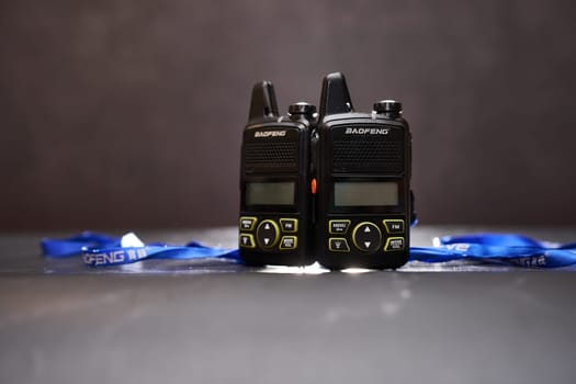 Two black Baofeng BF-T1 walkie-talkies with blue ribbons stand on a black table. High quality photo