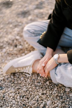 Girl sits with her hands crossed on her leg on a pebble beach. Cropped. Faceless. High quality photo