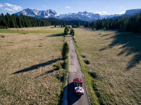 Groom drives bride in a white dress in a cabriolet along a mountain road. Drone. High quality photo