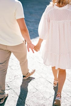 Man and woman walk holding hands along the paving stones. Back view. Cropped. High quality photo