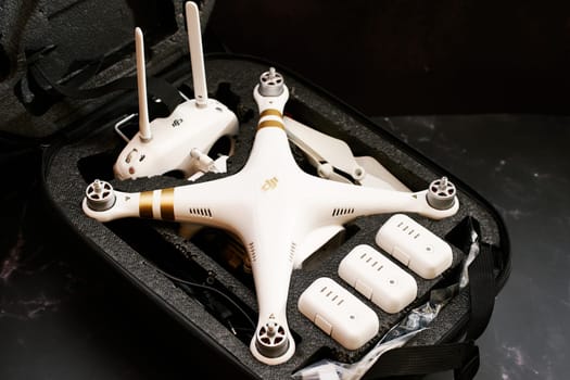 White DJI Phantom 3 drone with spare batteries and a control panel lies in a protective case on a black table. High quality photo