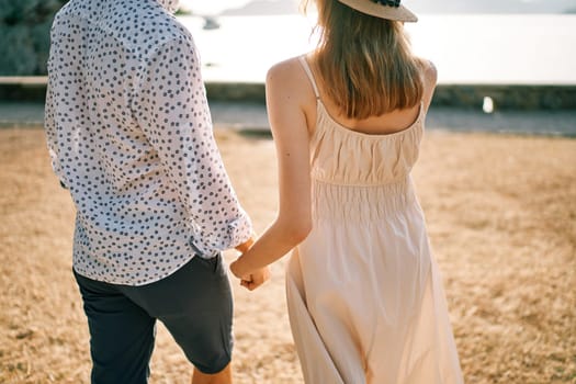 Man and woman walk along the seashore holding hands. Back view. Cropped. High quality photo