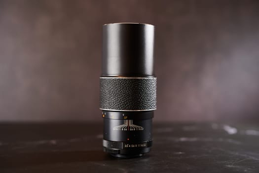 Vintage Chinon AutoZoom M42 telephoto lens stands on a black table. High quality photo