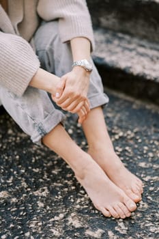 Barefoot girl sits with her hands folded in her lap on the stone steps. Cropped. Faceless. High quality photo