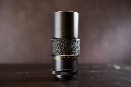 Vintage Chinon M42 telephoto lens stands on a black table. Caption: Lens made in Japan. High quality photo