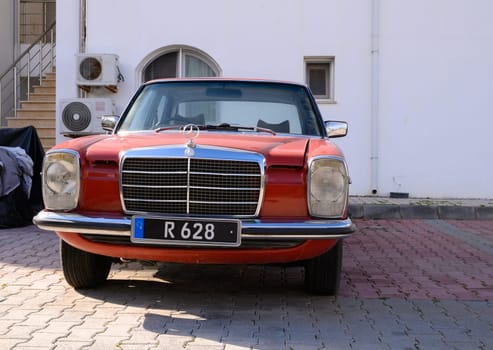 Gaziveren Cyprus -24.03.2025 A vintage red Mercedes vehicle is parked on a cobblestone surface, showcasing its elegant design and gleaming chrome details while basking in the afternoon sun near rustic architecture.