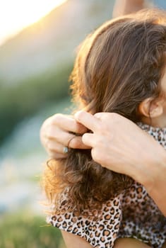 Mom braids the hair of a little girl. Close-up. Cropped. Faceless. High quality photo
