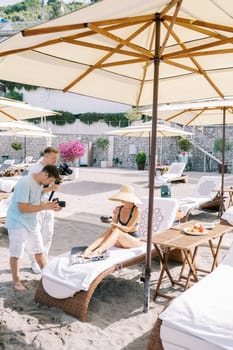 Photographers photograph woman sitting on a sun lounger on the beach with a plate of fruit. High quality photo