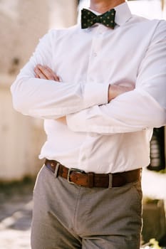 Torso of the groom with his arms crossed on his chest standing on the street. Cropped. Faceless. High quality photo